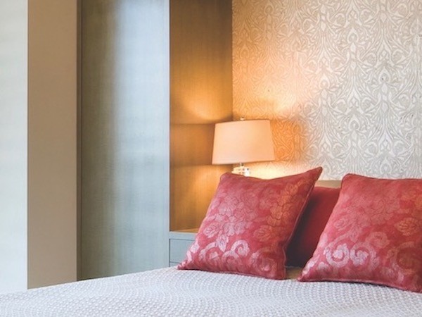 A bedroom with patterned wallpaper on the wall behind the bed.